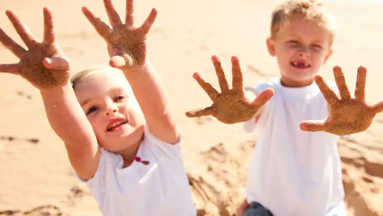 2 Kinder zeigen ihre sandigen Hände am Strand
