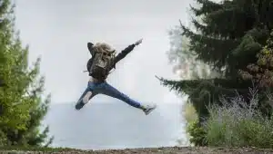 Frau mit Rucksack springt fröhlich in die Luft in der Natur