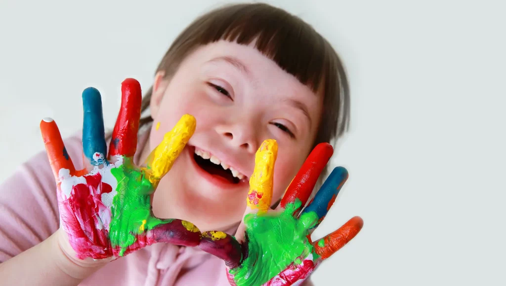 glückliches Mädchen mit besonderen Bedürfnissen zeigt farbige bemalte Hände