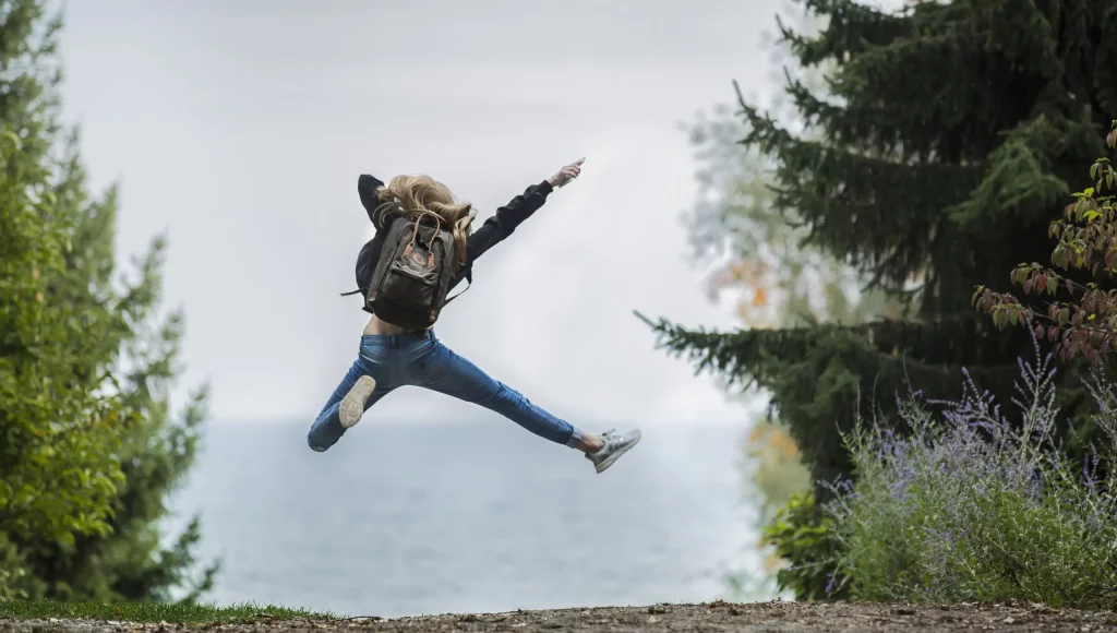 Frau mit Rucksack springt vor Freude in die Luft