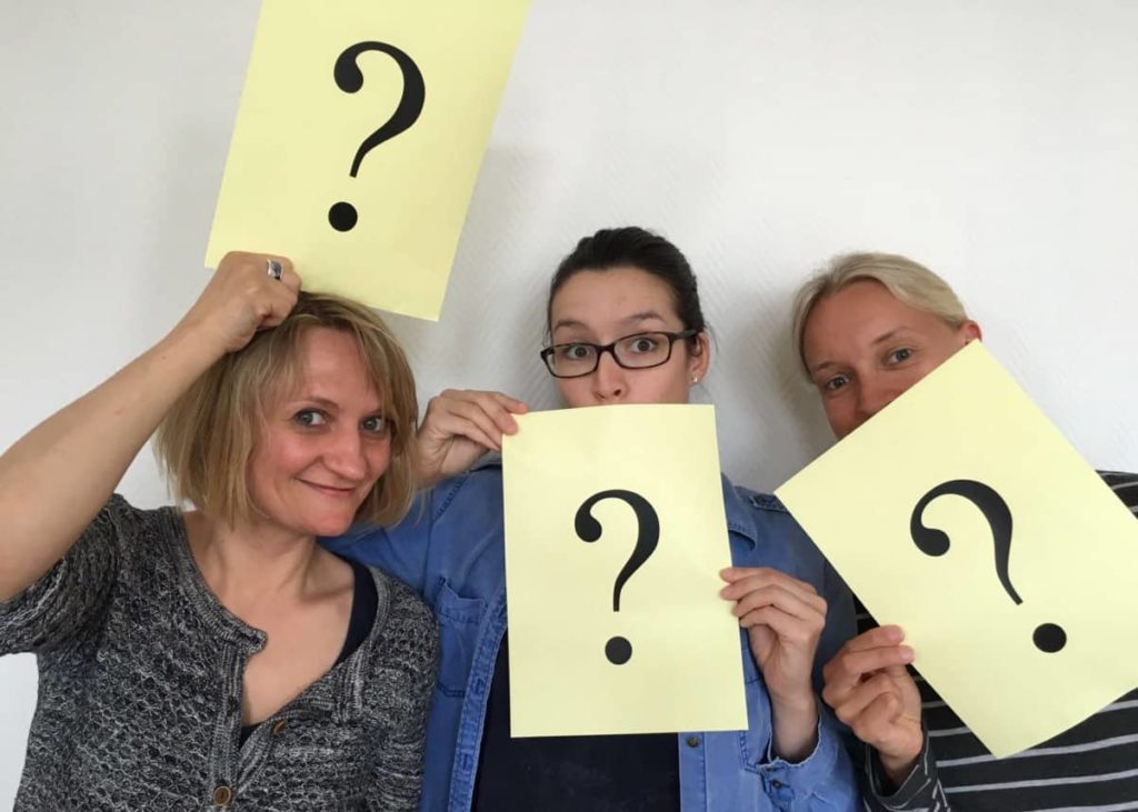 3 Frauen mit Papier, auf dem Fragezeichen zu sehen sind