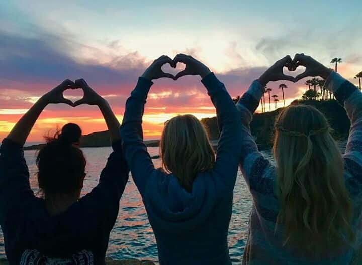 3 Frauen die mit ihren Händen Herzen vor dem Sonnenuntergang zeigen