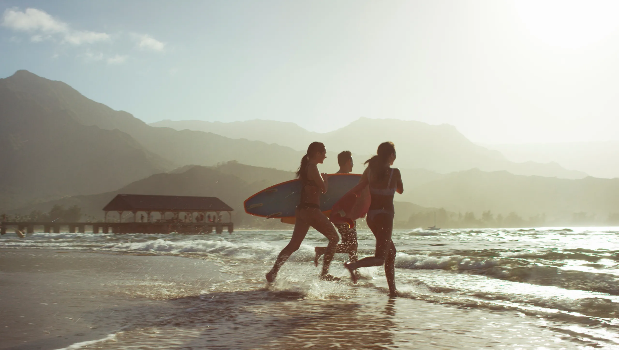 1 Mann und 2 Frauen laufen mit Surfboard ins wasser
