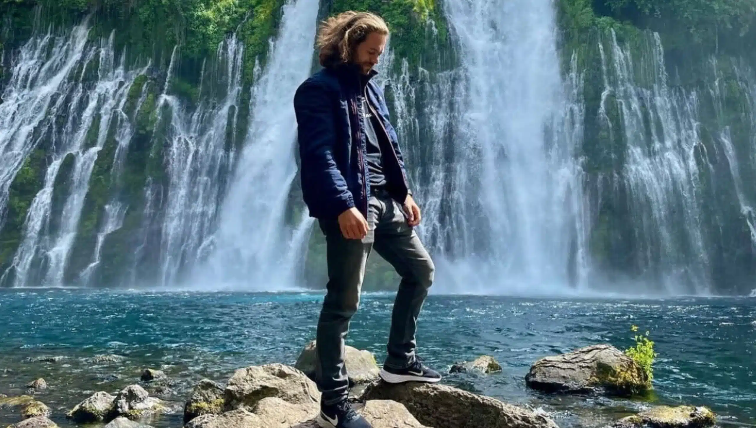 Mann steht auf Steinen vor Wasserfall